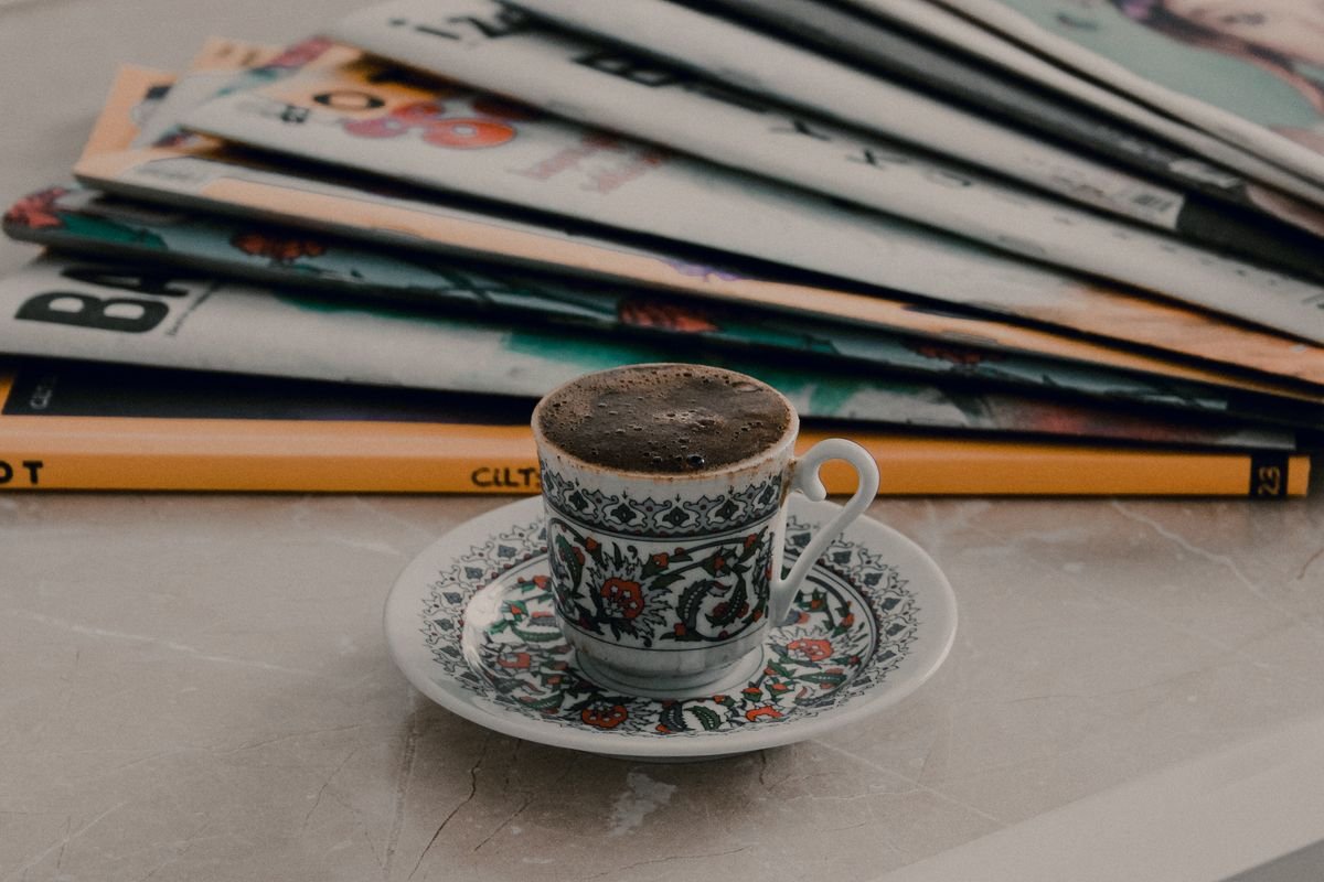 Decorative coffee cup placed on a marble table beside stacked magazines, creating a cozy morning vibe.